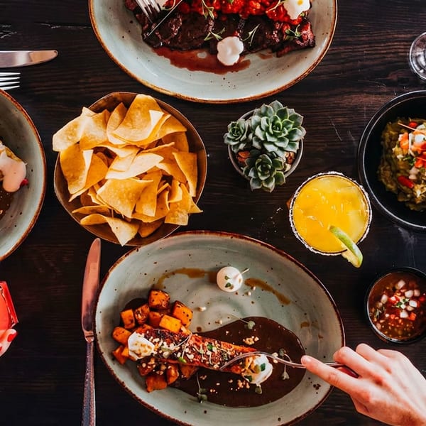 Overhead view of a dark wooden table laden with various Mexican dishes and cocktails.
