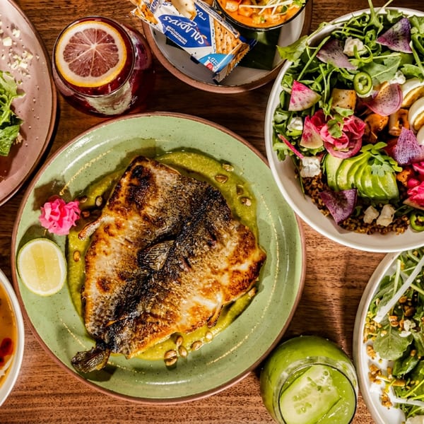 Overhead view of a wooden table laden with various colorful dishes, including salads, soup, and fish.