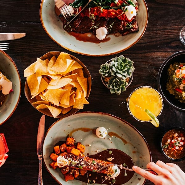 Overhead view of a dark wooden table laden with various Mexican dishes and cocktails.