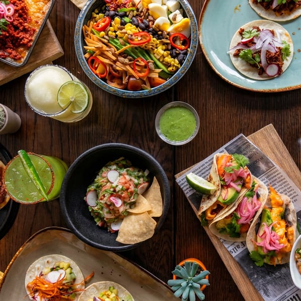 An overhead view of a wooden table laden with various Mexican dishes, including tacos, dips, and drinks.