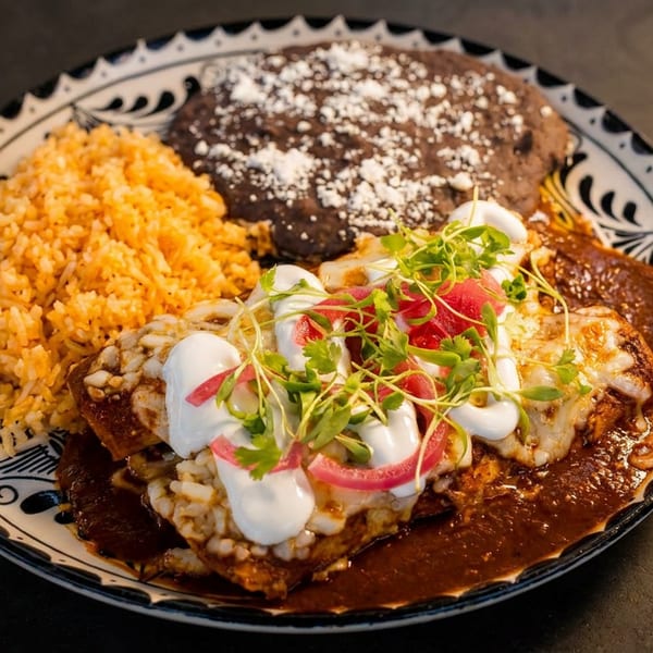 Mexican dish with enchiladas, rice, and refried beans on a decorative plate.