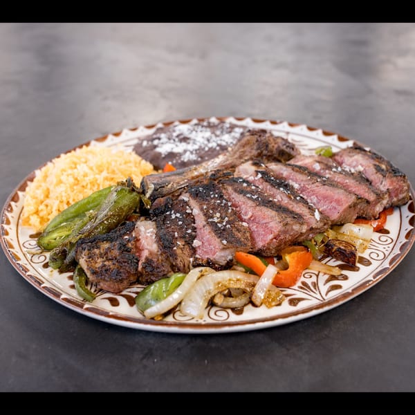 Grilled steak, sliced and seasoned, with rice, beans, and sautéed vegetables on a decorative plate.